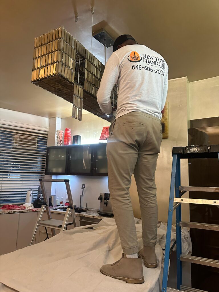 Technician installing modern chandelier from New York Chandeliers, wearing branded shirt