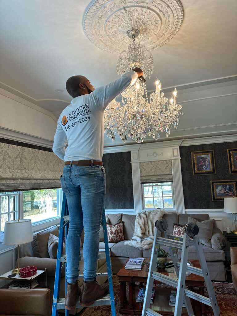 Person on ladder repairing crystal chandelier in elegant living room
