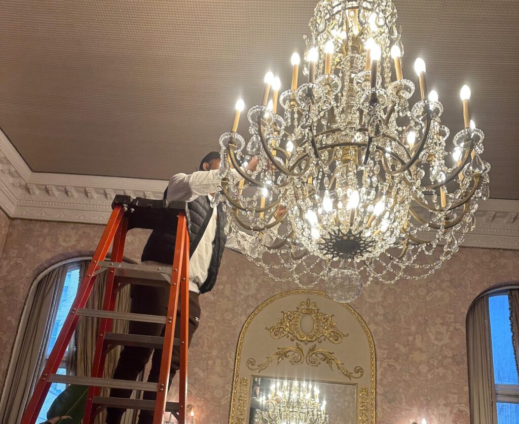 Technician installing a large crystal chandelier in a New York City building. Chandelier repair and installation services by new york Chandelier Services