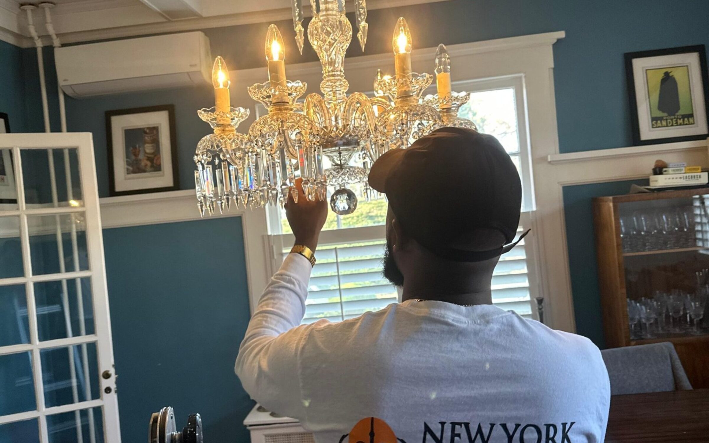 Technician adjusting chandelier in a room with "New York Chandelier" shirt