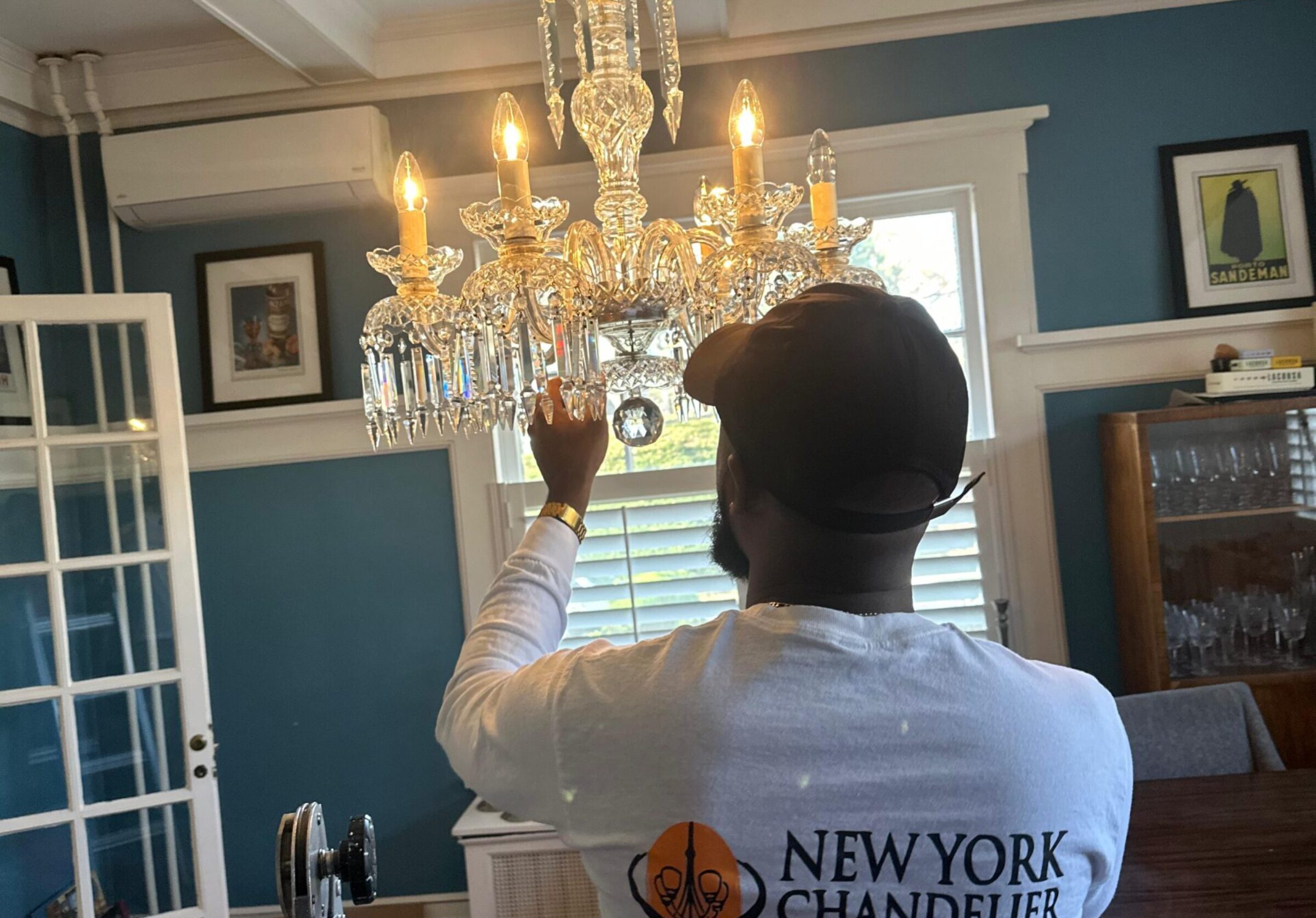 Technician adjusting chandelier in a room with "New York Chandelier" shirt