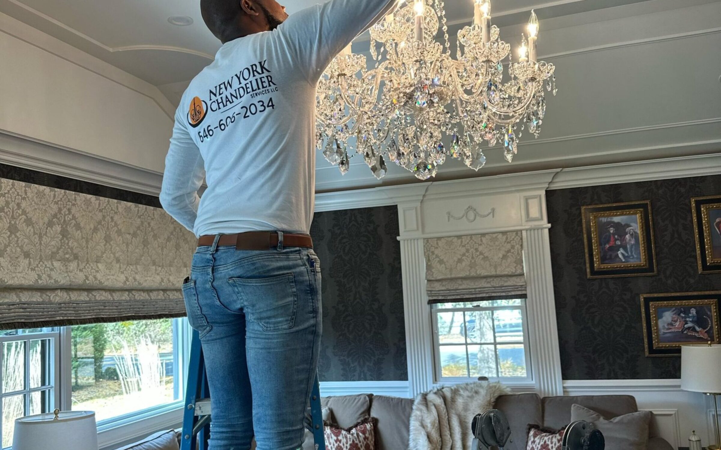 Person on ladder repairing crystal chandelier in elegant living room