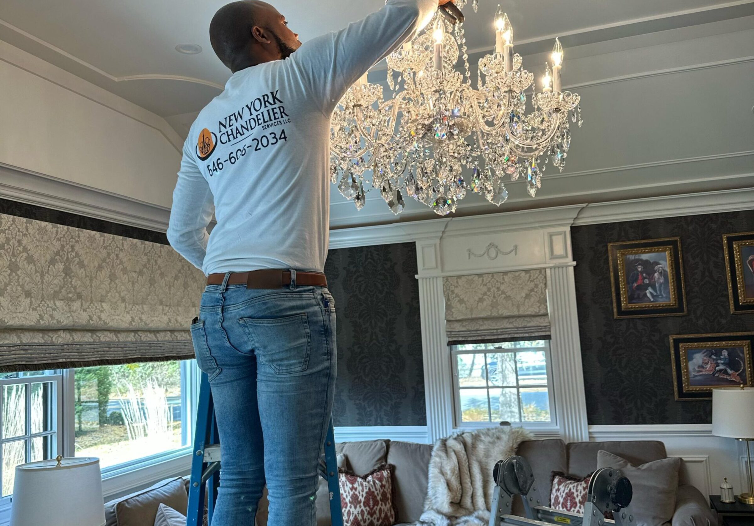 Person on ladder repairing crystal chandelier in elegant living room
