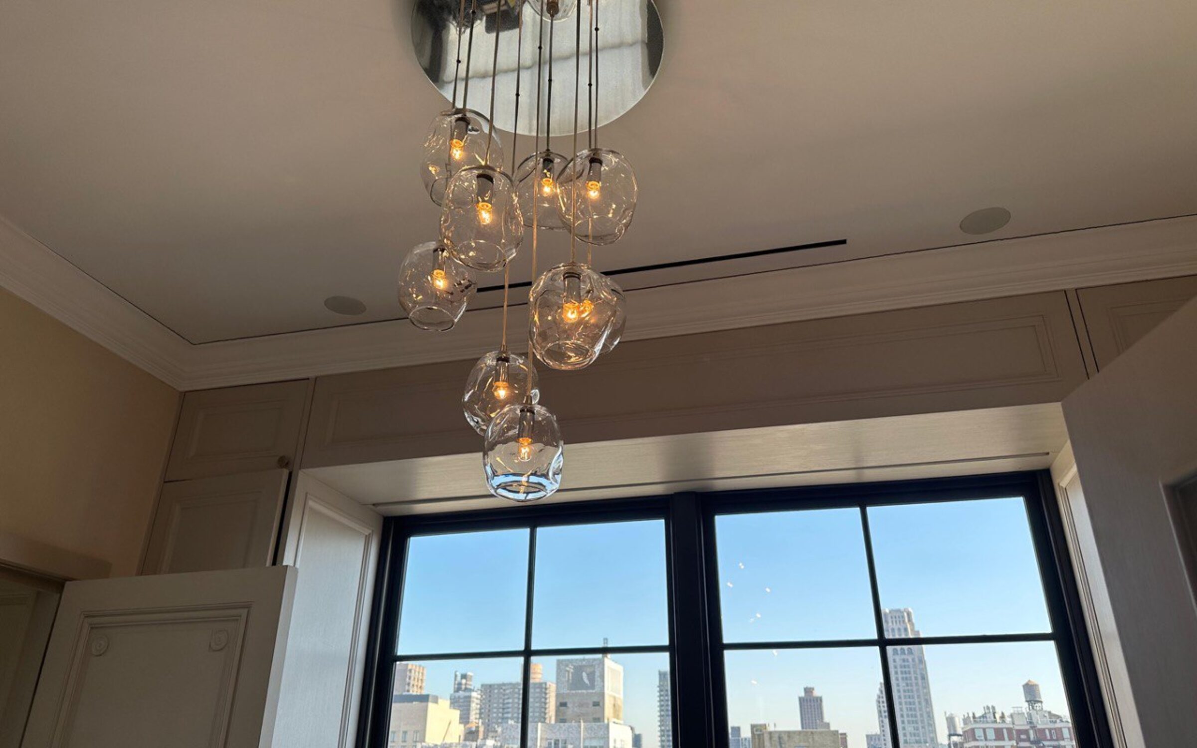 Modern glass chandelier illuminates NYC view. New York chandelier services.